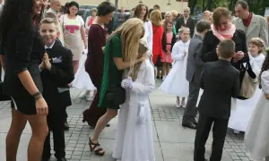 Dzieci w strojach komunijnych i dorośli na zewnątrz.
