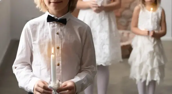 Dzieci w białych strojach trzymają zapalone świece podczas Komunii Świętej.